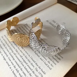 Gold and silver textured spiral open bangles with unique folded patterns on a book.