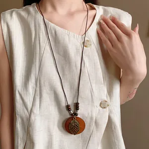 Ethnic style long necklace with circular wood pendant and metal leaf cutout detail.