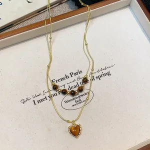 Close-up detail of a layered gold-tone necklace with tiger eye beads and heart pendant