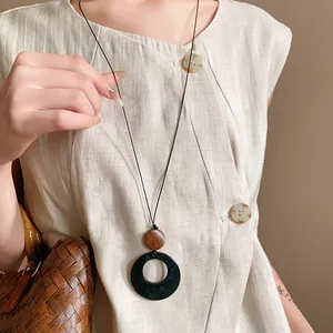 Detail of retro ethnic long necklace with black circular hollow pendant and wooden bead.