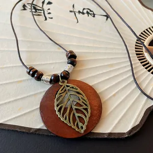 Close-up of vintage ethnic necklace with round wood pendant and hollow bronze leaf charm