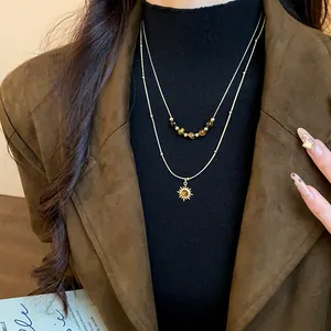 Detail of layered gold necklace with tiger eye beads and sun pendant
