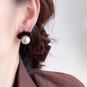 Detail view of elegant brown flocking bow and white pearl stud earrings on a model