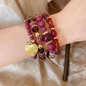 Macro view of multi-layer beaded bracelet set featuring an engraved golden heart charm