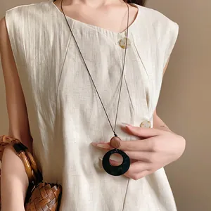 Close-up of the circular black pendant and wood bead detail of an ethnic necklace.