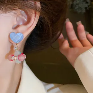 Close-up of cute colorful glass heart drop earrings with silver needle shown on ear