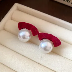 Close-up of elegant flocked red velvet bow and pearl stud earrings on a display tray.
