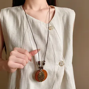 Vintage ethnic style necklace with circular wooden pendant and hollow metal leaf charm.