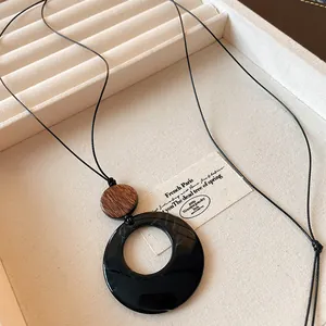 Detail shot of an ethnic style long necklace with a hollow round black pendant and wooden accent