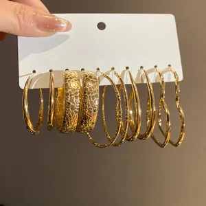 Close-up detail of six pairs of various textured gold-toned earrings on a white card