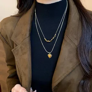 Close-up of a double-layered tiger eye bead necklace with a heart pendant on a model
