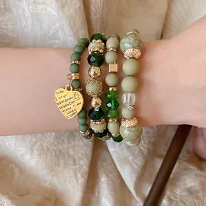 Close-up detail of bohemian beaded bracelet set with green crystals and golden heart pendant
