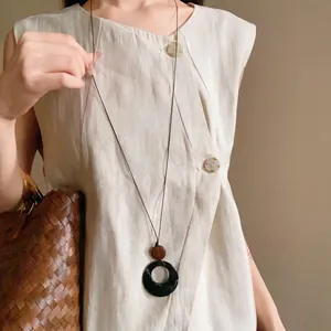 Close-up of ethnic style long necklace featuring a circular pendant on a linen dress.