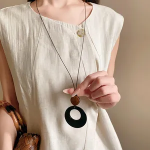 Detail view of retro ethnic long necklace with black circular pendant and wood accent