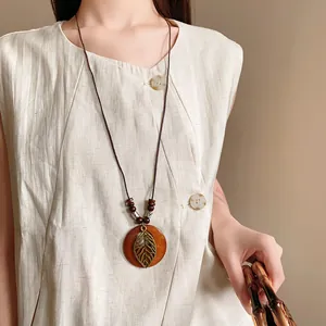 Close-up of ethnic round wooden necklace with hollow leaf pendant on linen vest