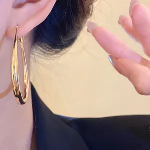 Close-up view of elegant minimalist gold oval hoop earrings being worn by an Asian model