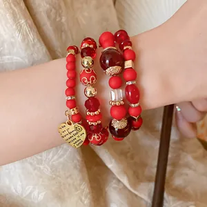 Detailed close-up of red beaded bracelet with engraved heart charm and gold accents