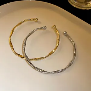 Minimalist twisted open bangles with hammered texture in gold and silver finish.