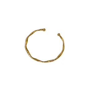 Minimalist geometric twisted gold open bangle featuring a hammered texture design