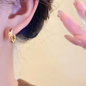 Detail shot of elegant gold twisted hoop earrings with textured finish on model's ear