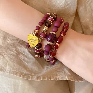 Detail shot of multi-layered purple beaded bracelet with engraved gold heart charm