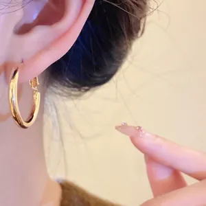 Close-up of minimalist gold hoop earring worn on ear with soft warm lighting.