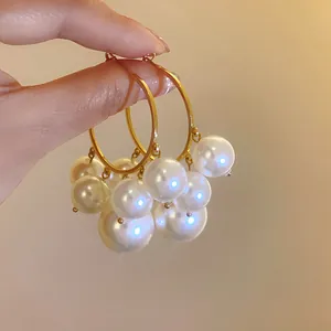 Nahaufnahme eleganter goldener Creolen mit kaskadierenden weißen Perlen in der Hand