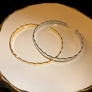 Detail shot of wavy gold and silver minimalist open cuff bracelets on a white plate
