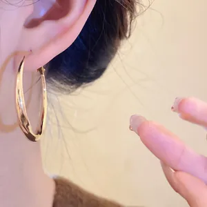 Close-up detail of a minimalist gold twisted hoop earring worn on the ear