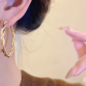 Detailed close-up view of a gold-colored twisted hoop earring styled on a model's ear