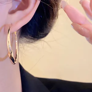 Macro view showing the elegant twisted detail of a gold hoop earring on a model's ear