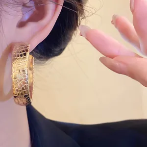 Close-up detail of textured gold hoop earring with hammered scale pattern on model's ear.
