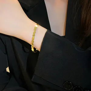 Close-up detail of a minimalist geometric gold open bangle styled with a black blazer