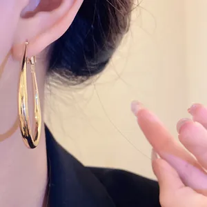 Close-up of gold-plated twisted hoop earrings worn on ear for a retro minimalist look.