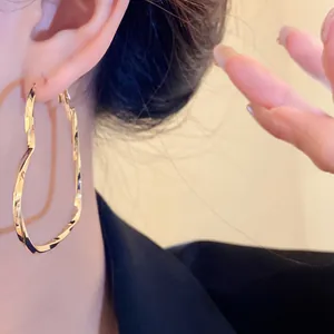 Elegant large gold twisted heart hoop earrings shown on a model's ear