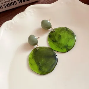Gros plan de boucles d'oreilles pendantes en résine vert forêt sur une assiette