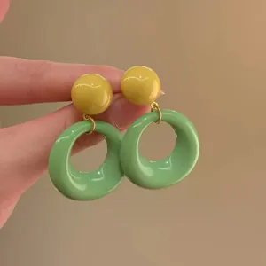 Detail view of retro contrast color earrings featuring a yellow stud and green round ring
