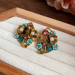 Dettaglio di orecchini vintage a forma di fiore con cristalli colorati e perle.