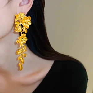 Detailed macro view of elegant matte gold floral and leaf tassel drop earring on model
