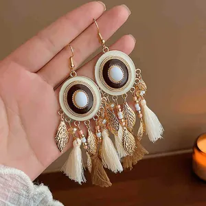 Close-up detail of Bohemian tassel earrings featuring golden leaves and soft fabric fringes.