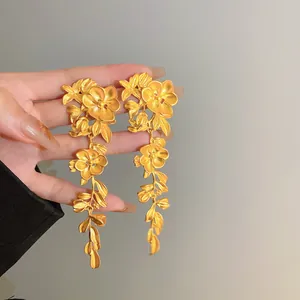 Detailed close-up of vintage-style matte gold floral and leaf tassel drop earrings.