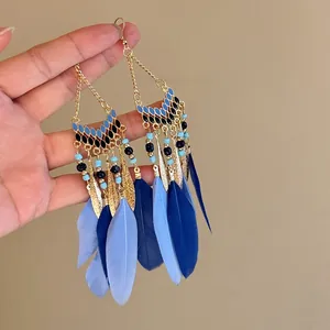 Close-up view of Bohemian blue feather tassel earrings with gold chains and beads.