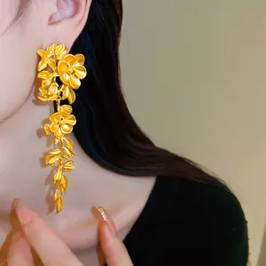 Detail showing elegant long matte gold floral and leaf tassel earrings on a model