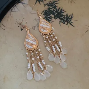 Detailed view of bohemian gold tassel earrings with white beads and teardrop charms.