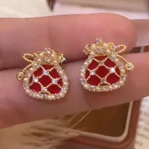 Macro detail view of gold-plated lucky pouch earrings with red enamel, pearls and zirconia
