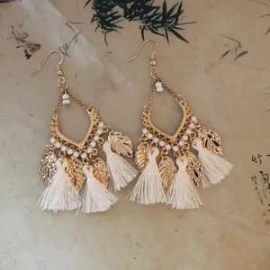Macro view of vintage bohemian tassel earrings featuring gold leaf charms and white beads