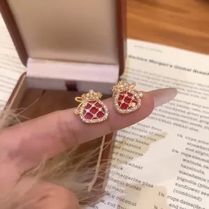 Detail view of gold-plated fortune bag earrings with red zircon and pearls on hand.