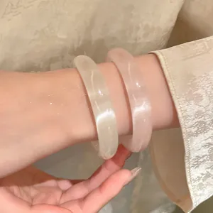 Macro detail of translucent resin round bangles in white and pink on a model's wrist