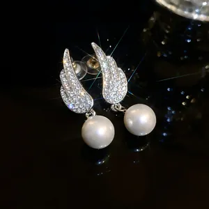 Close-up of elegant wing-shaped earrings with rhinestones and white pearls