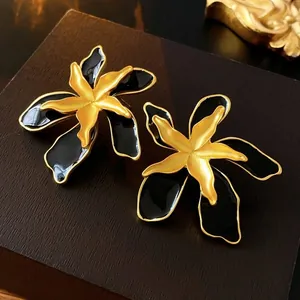Elegant vintage black and gold floral stud earrings with premium enamel finish on wood background